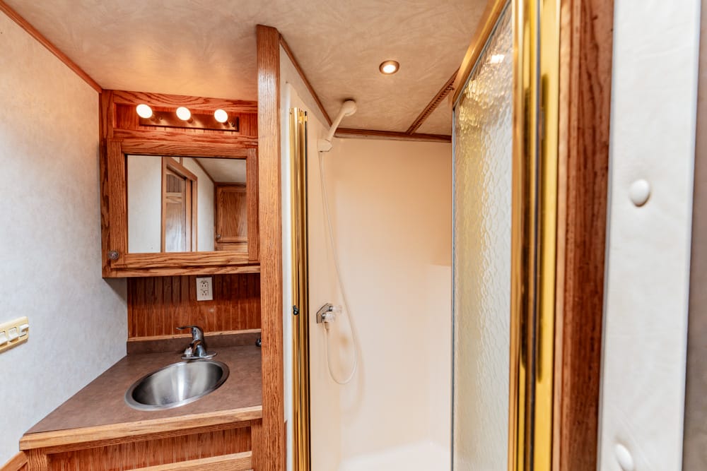 Compact RV bathroom featuring a wood vanity, stainless sink, mirror, and a separate shower with a glass door.