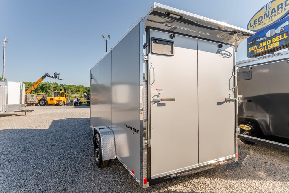 Silver, enclosed cargo trailer with double rear doors on a gravel lot, other trailers visible in the background