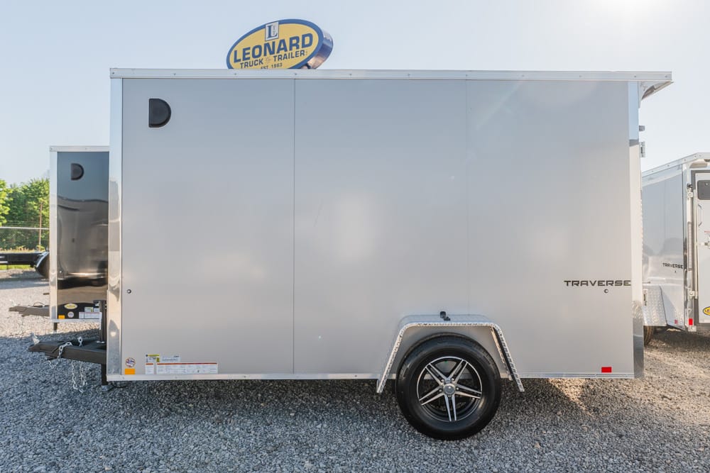 Silver enclosed cargo trailer with single axle, parked on gravel lot; rear hitch and wheel well visible; Leonard Truck & Trailer sign on top edge.
