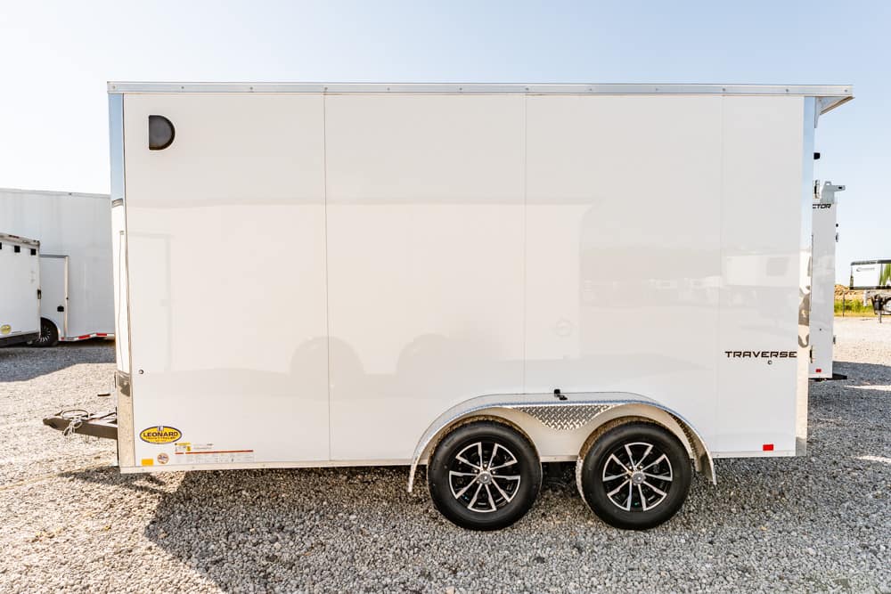 White enclosed cargo trailer with two-axle wheels parked on gravel, side view showing curved wheel arches and diamond-plate fender trim (Traverse logo visible).