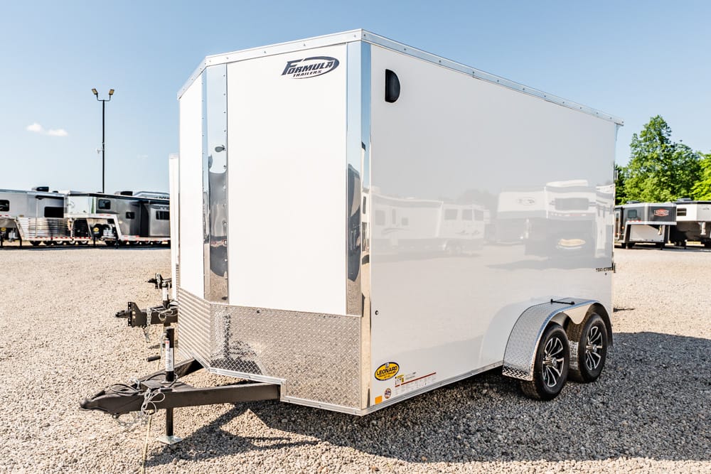 White enclosed cargo trailer with dual axles and diamond-plate front on a gravel lot, Formula Trailers branding visible.