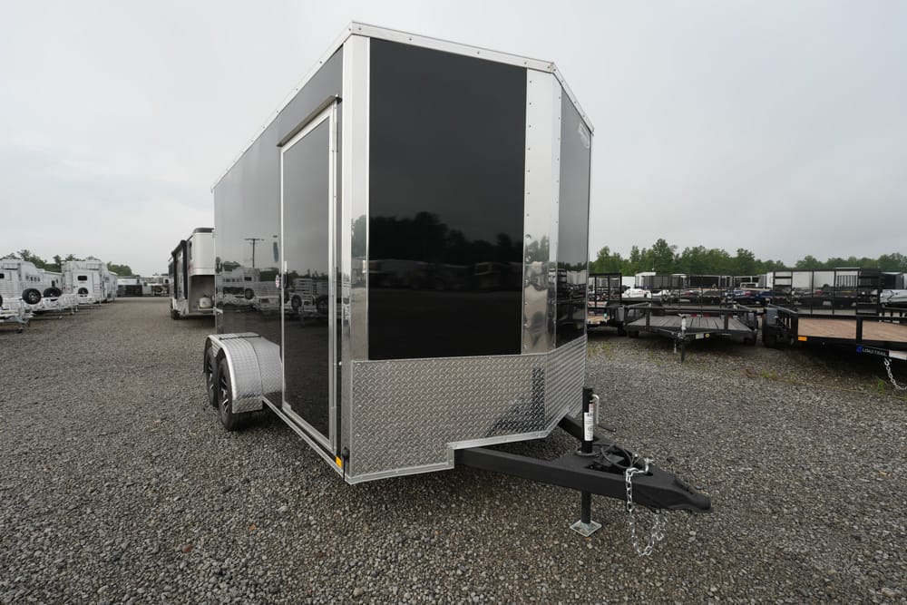 Front view of a black enclosed cargo trailer with diamond-plate front, parked in a gravel trailer lot.