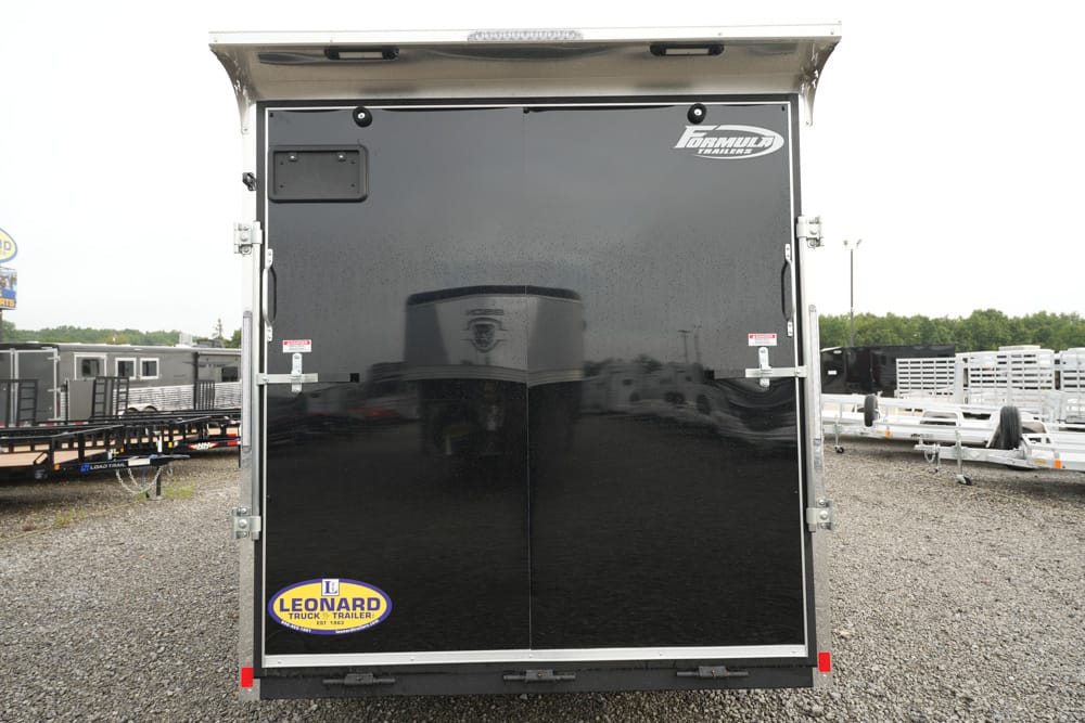 Rear view of a black enclosed cargo trailer with a Leonard sticker on the lower left and a shiny double door exterior in a trailer yard.