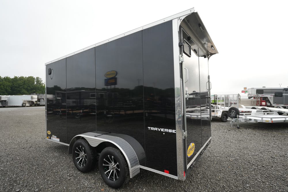 Black opaque, two-axle enclosed trailer with diamond-plate wheel arches and 'TRAVERSE' branding in a gravel lot.