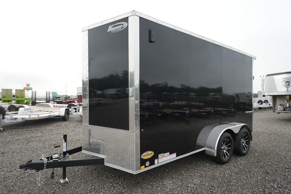 Black enclosed cargo trailer with tandem axles and diamond-plate front on a gravel lot.