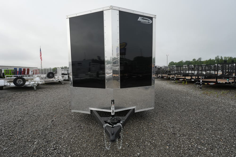 Front view of a black-and-silver enclosed cargo trailer with diamond-plate tongue on a gravel lot, hitch and safety chains visible.