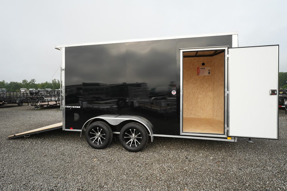 Black enclosed trailer with open rear door and ramp, showing a wooden interior and dual axles with black rims (trailer for transport/storage). Perhaps used for hauling gear or vehicles.