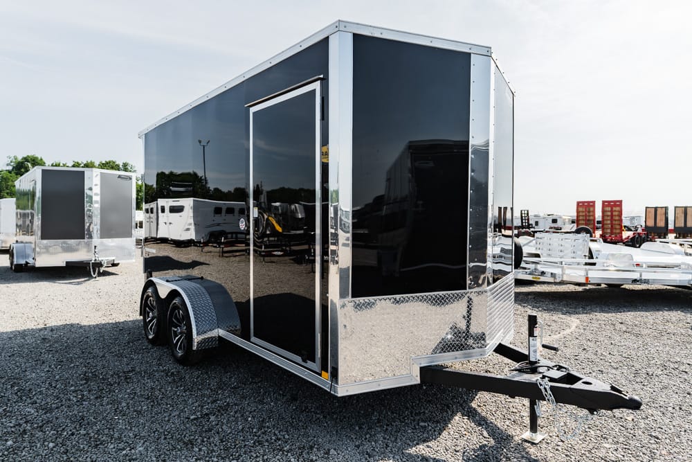 Black enclosed utility trailer on a dual-axle chassis with diamond plate trim and a front hitch, parked on a gravel lot.