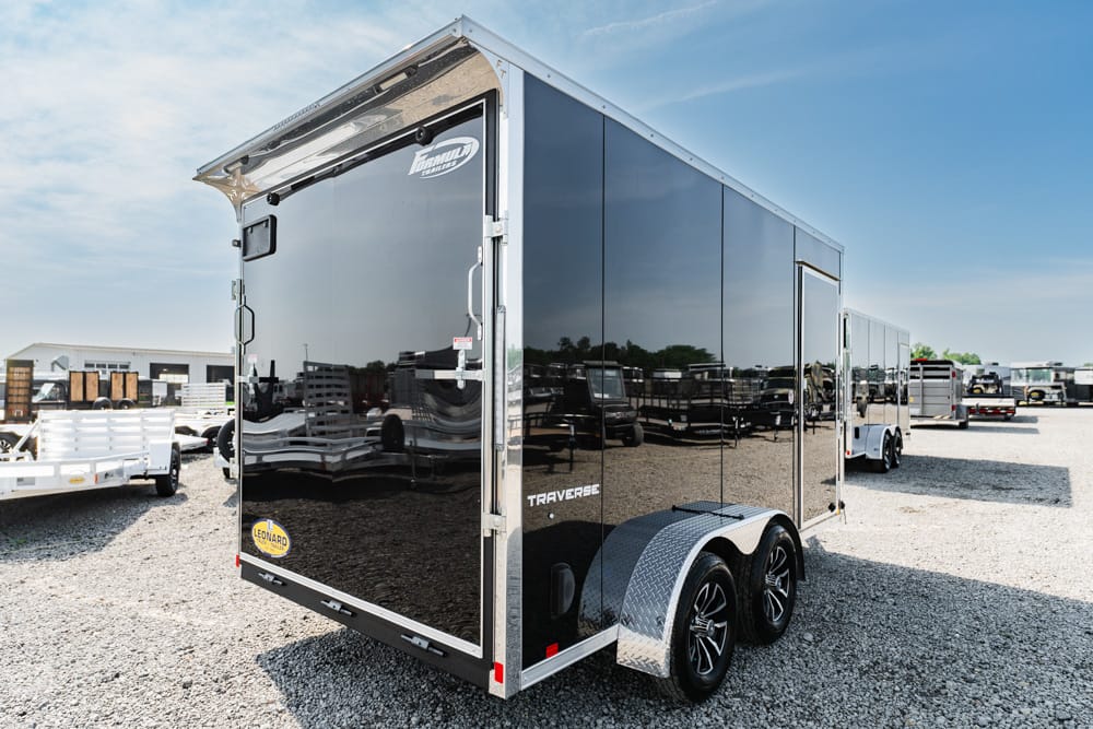 Shiny black enclosed cargo trailer with dual axles and diamond plate fenders in a gravel dealership lot.