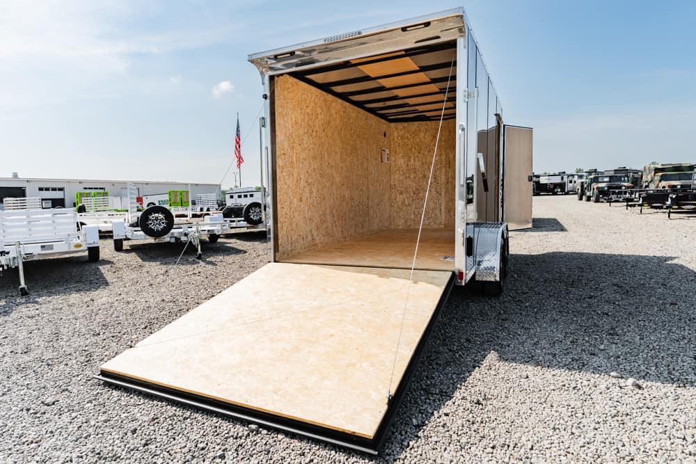 Open empty cargo trailer with ramp down, in a gravel lot among other trailers in the background.