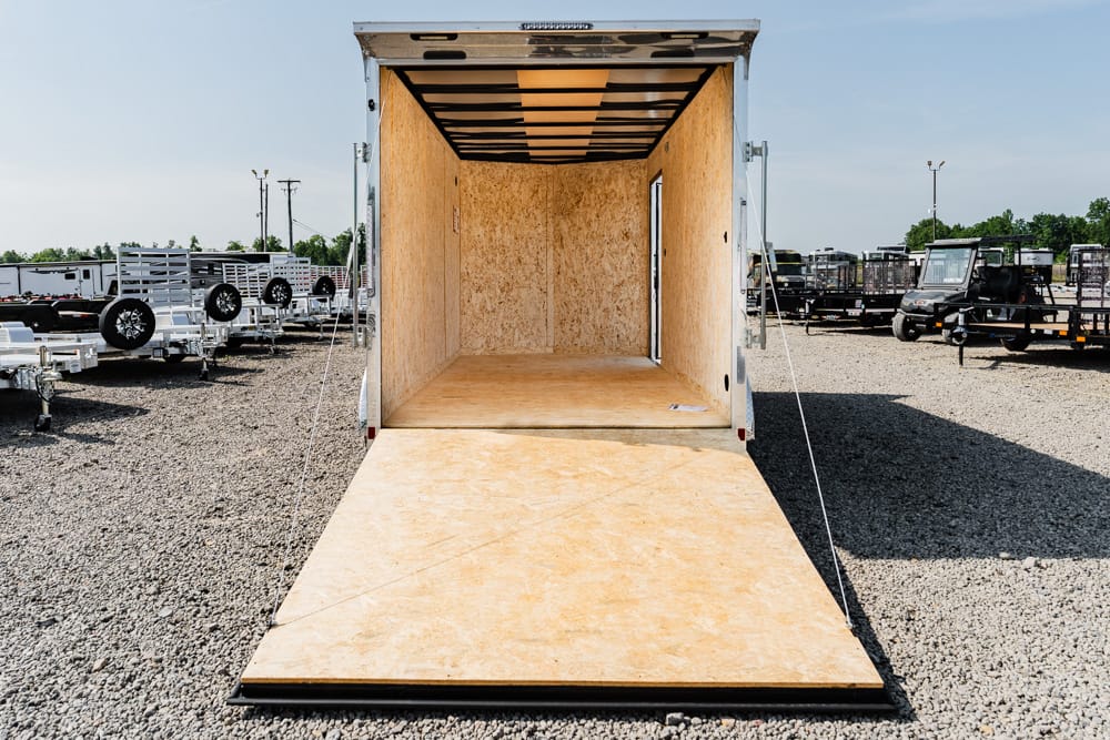 Open cargo trailer with a wooden ramp extending to a gravel lot, ready for loading goods