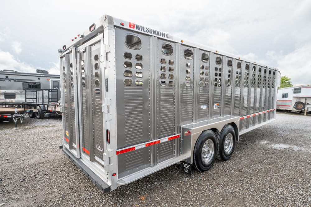 Long silver livestock trailer with ventilation holes along each stall, parked on gravel. (Informative)