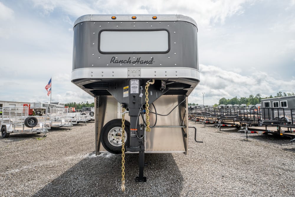 Front view of a silver Ranch Hand gooseneck horse trailer in a gravel trailer lot with other trailers nearby.