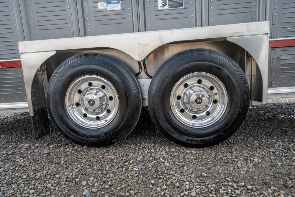 Dual trailer wheels with chrome rims and black Hankook tires under a metal fender on gravel.