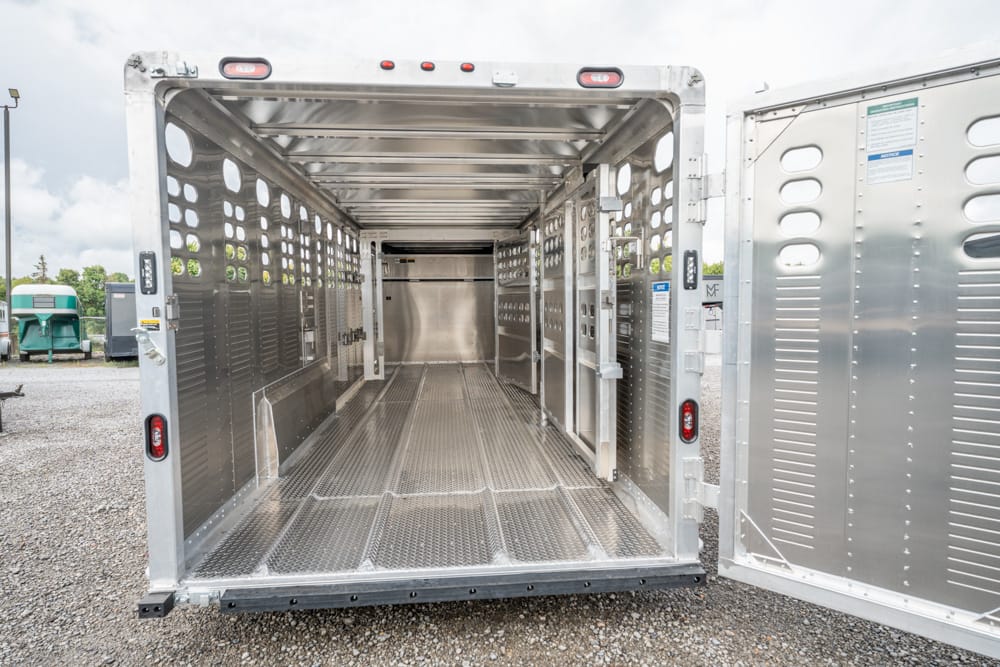 Empty aluminum livestock trailer interior with ventilated side walls and diamond-plate floor, doors wide open.