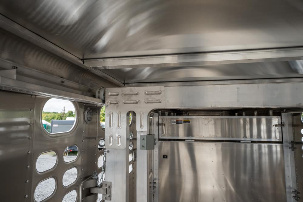 Interior of a silver aluminum trailer with riveted panels and rounded windows along the sides, showing a reinforced doorway.