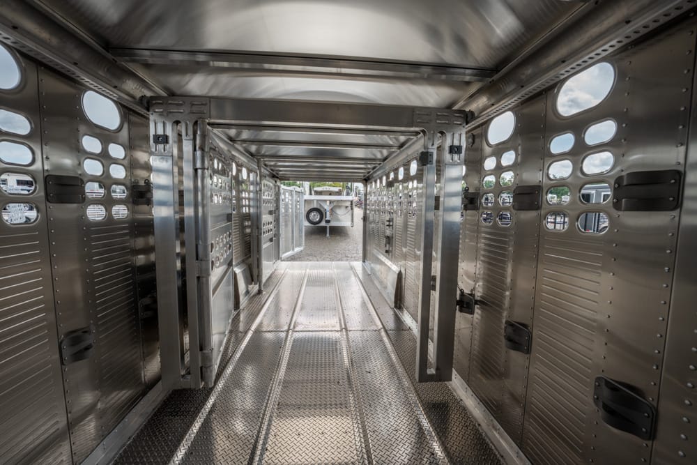 Interior of a stainless steel livestock trailer with a central walkway and side partitions.