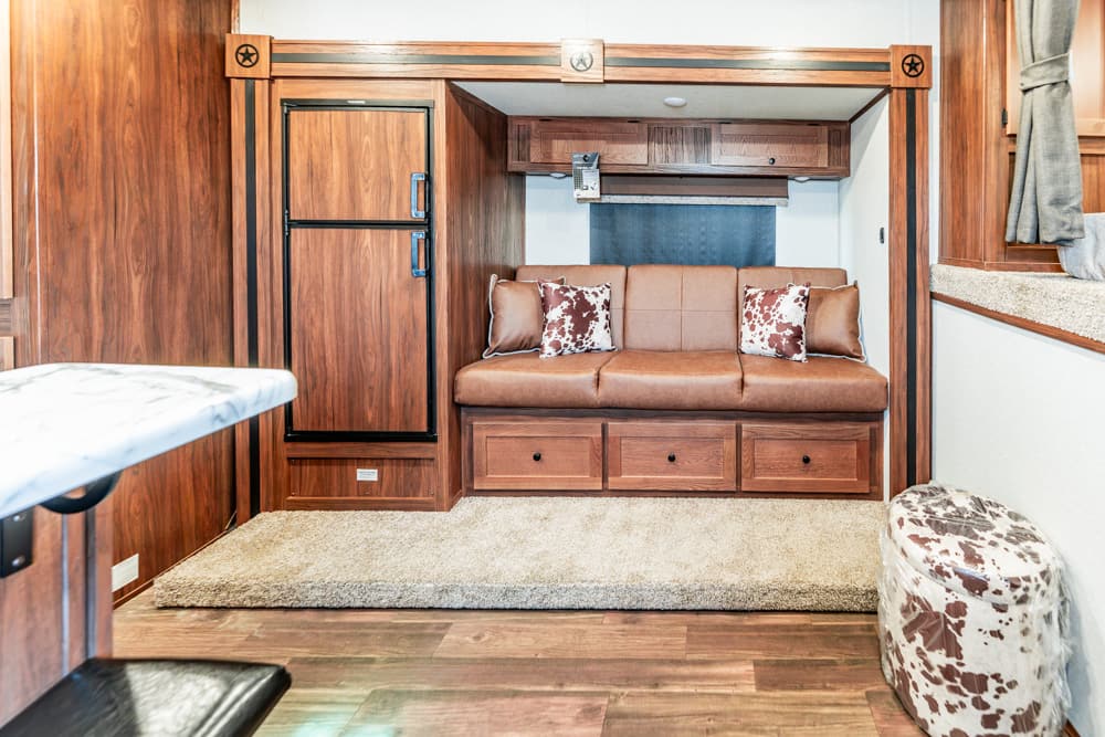 Compact RV living area with brown leather sofa, overhead cabinets, and built-in storage drawers beneath the seat.