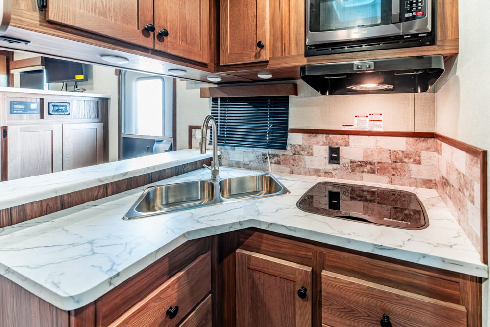 RV kitchen with marble counter, double sink, glass-cover stove, wooden cabinets, and a mounted microwave above.