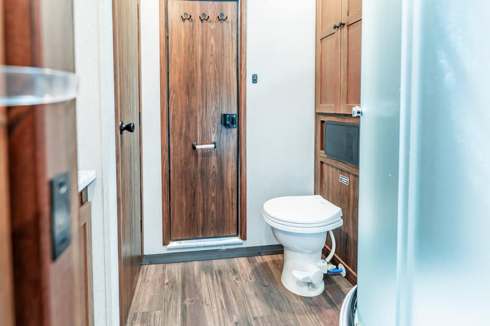 Compact bathroom with wood-paneled doors, a white toilet, and built-in cabinets—likely in an RV or small space