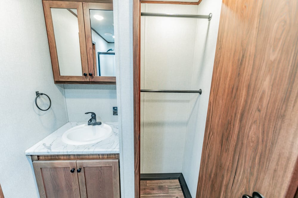 Compact bathroom vanity with marble countertop, oval sink, and wooden cabinet; towel ring on the wall to the left and mirrored cabinet above.