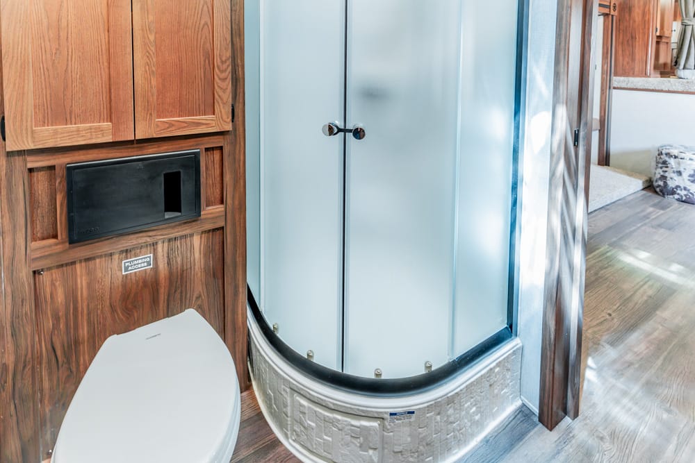 RV bathroom with wooden cabinets, a white toilet, and a curved glass shower enclosure.