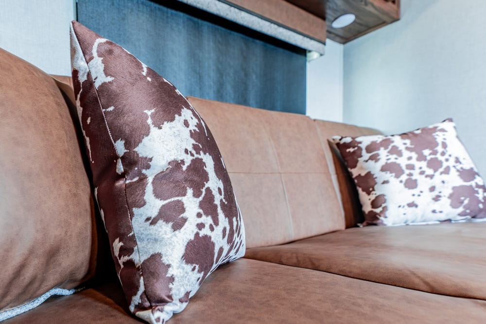 Brown suede sofa with cowhide-pattern throw pillows in a modern living room setting.