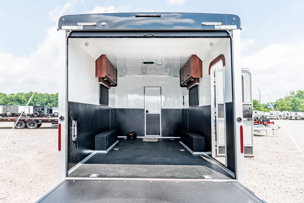 Interior of an empty trailer with black lower walls, white upper walls, and two wooden cabinets above bench seating along both sides.