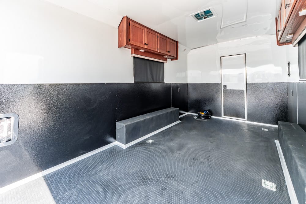 Interior of a utility trailer with a bench seat, dark wainscoting, and upper wooden cabinets