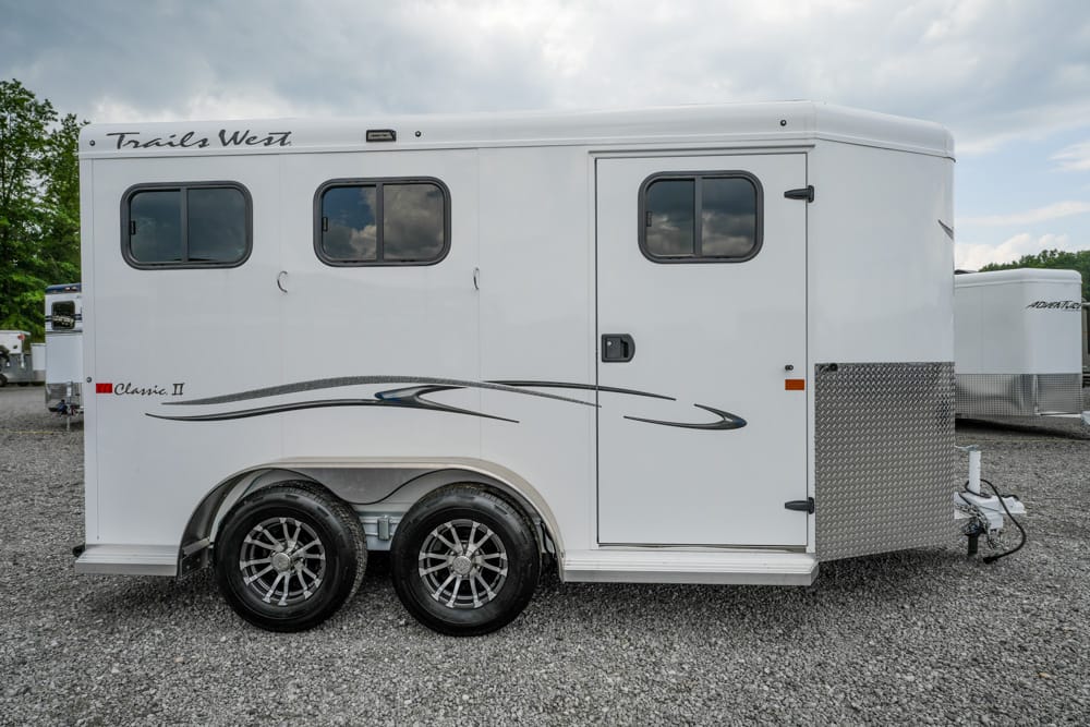 White Trails West Classic II horse trailer with two side windows and decorative black swoosh graphics on a gravel lot.