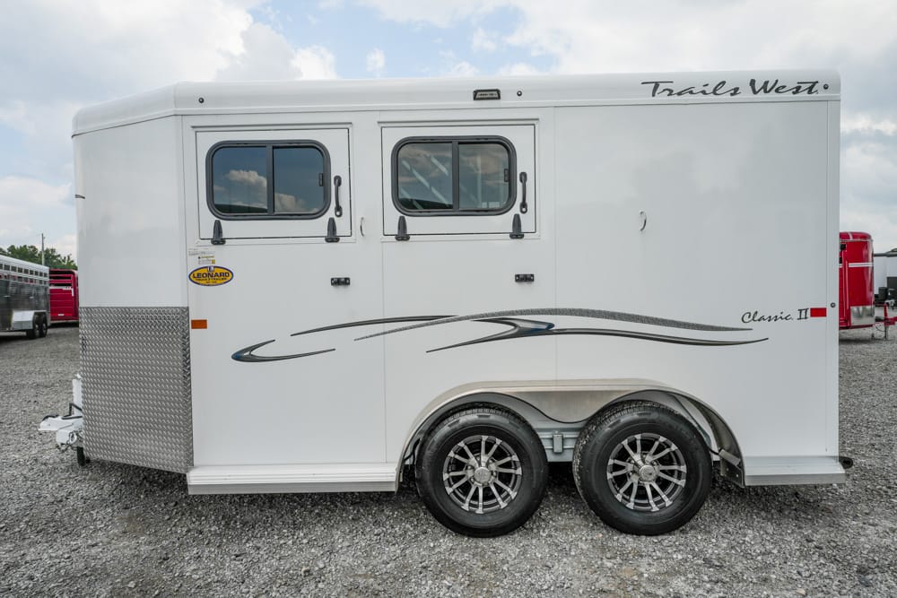 White Trails West horse trailer seen in profile with two windows and chrome wheels on gravel.