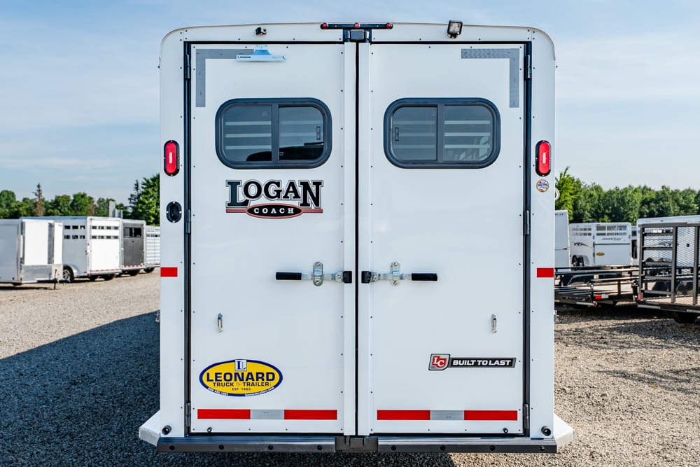 Rear view of a white Logan Coach trailer with two doors, small windows, and branding visible on back doors.