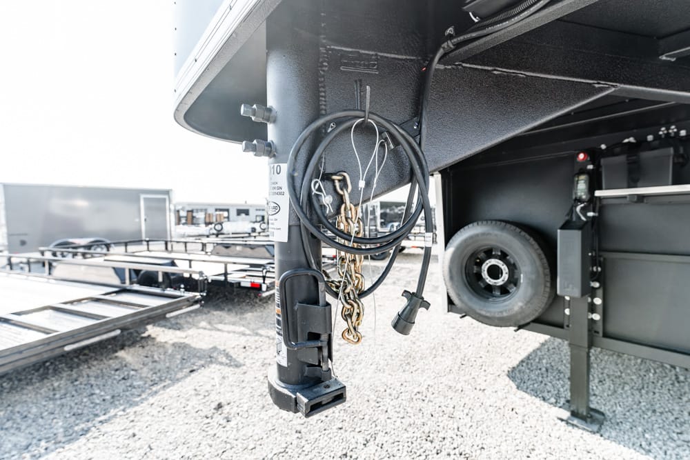Close-up of a trailer hitch area with coiled cables, hanging chains, and a padlock on a vertical support; spare tire visible in background.