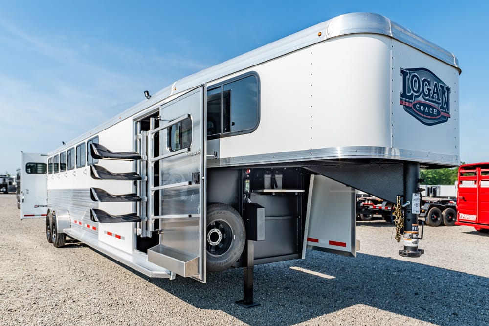 Logan Coach horse trailer with side storage compartments and fold-out steps on a gravel lot.