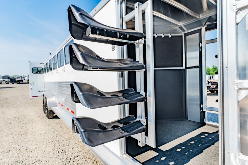 White horse trailer with four black saddle racks mounted on the side; open rear interior visible.