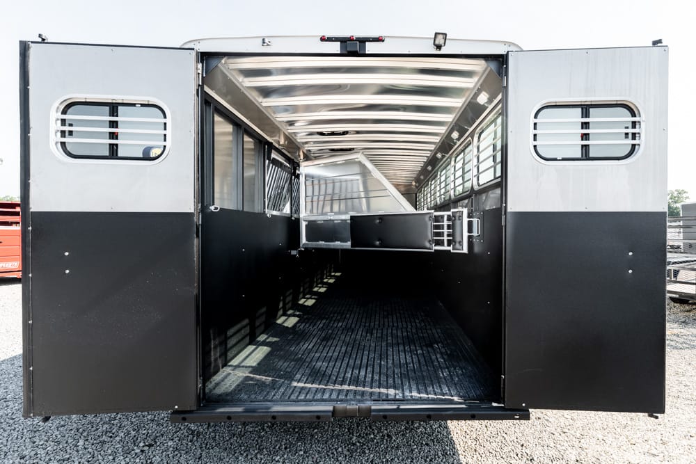 Open horse trailer at the back with wide doors, empty interior, black lower panels, metal walls, and a center divider under daylight.