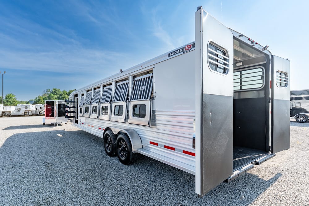 White livestock trailer with side vents and open rear ramp, parked on a gravel lot under a blue sky