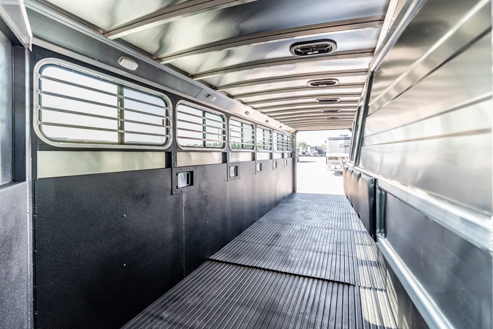 Interior of a metal transport trailer with ventilated side windows and a ribbed floor, viewed from the back corridor