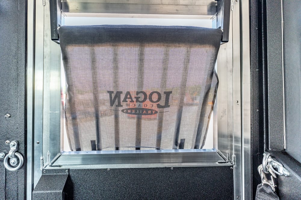 Interior view of an industrial machine showing a black mesh bag hanging inside a metal frame and chute system, used for packaging or processing machinery.