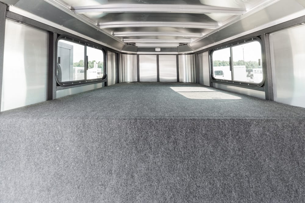 Interior of an empty trailer with a raised carpeted platform and large side windows on both sides.
