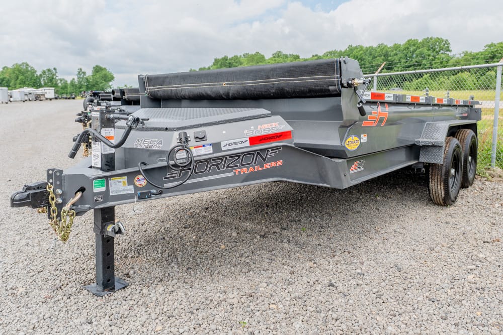 Heavy-duty gray flatbed trailer with dual axles and Horizon Trailers branding on a gravel lot at an outdoor storage yard.