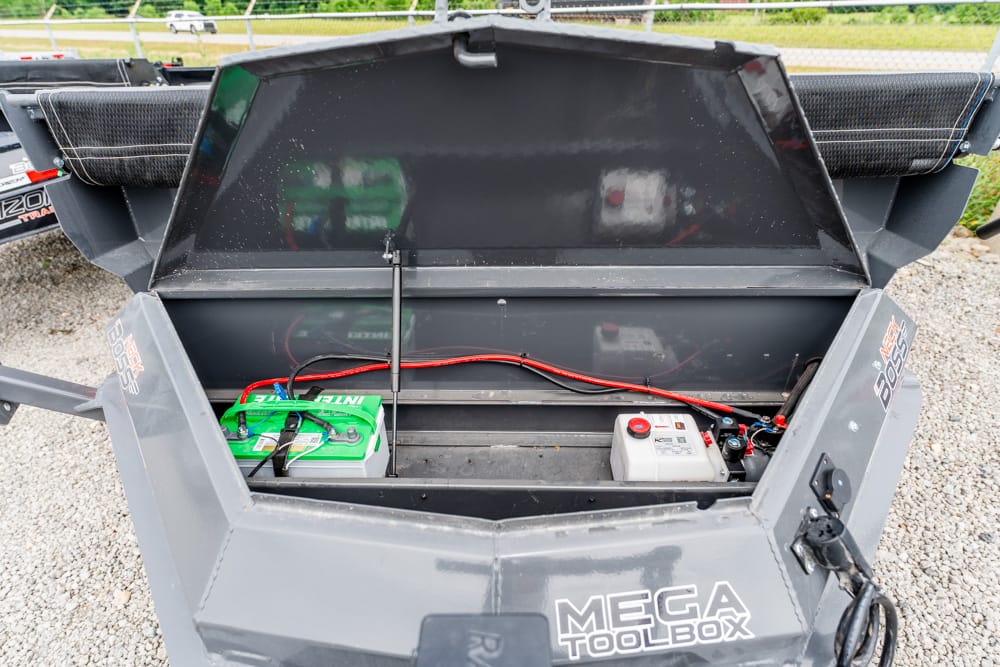 Open Mega Toolbox showing a green battery, red and black jumper cables, and a white container inside on a gravel surface