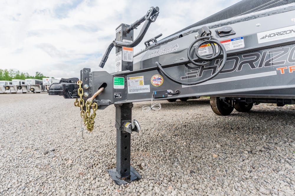 Front end of a gray Horizon boat trailer with a raised jack leg, safety chains, and electrical cords on a gravel lot.