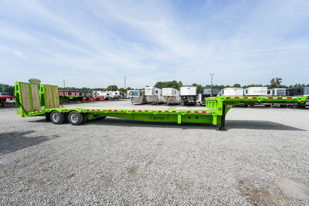 Bright green lowboy trailer on a gravel lot with other trailers in the background, ready for hauling heavy equipment.