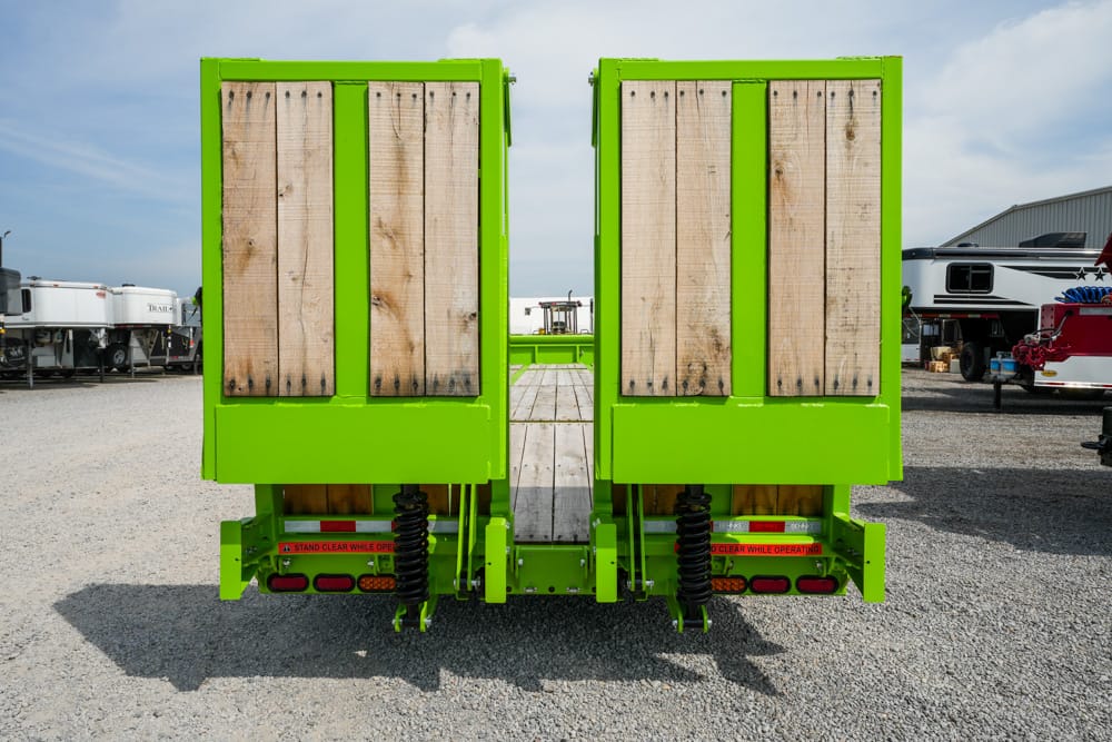 Bright green dual-split trailer ramps with wooden planks, parked on a gravel lot with RVs in the background.