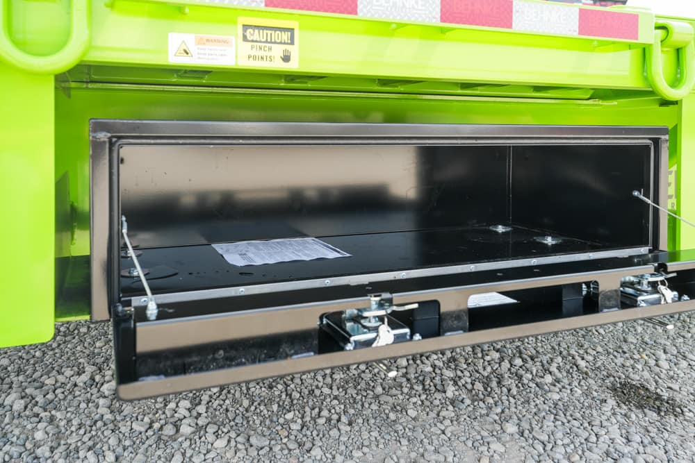 Open side storage compartment on a bright green utility vehicle, revealing a black metal tray and metal latches/dowels inside.