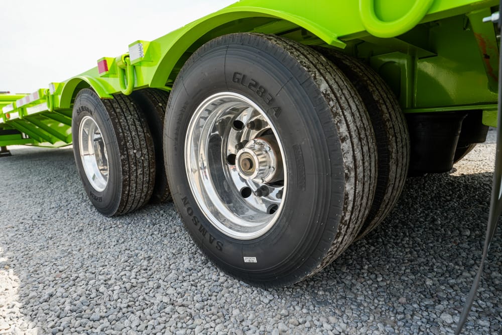 Close-up of a bright green heavy-duty trailer with chrome wheels and multiple rear axles on gravel surface