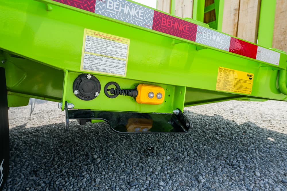 Close-up of a bright green trailer rear with a yellow remote control and hydraulic connections on a gravel surface.