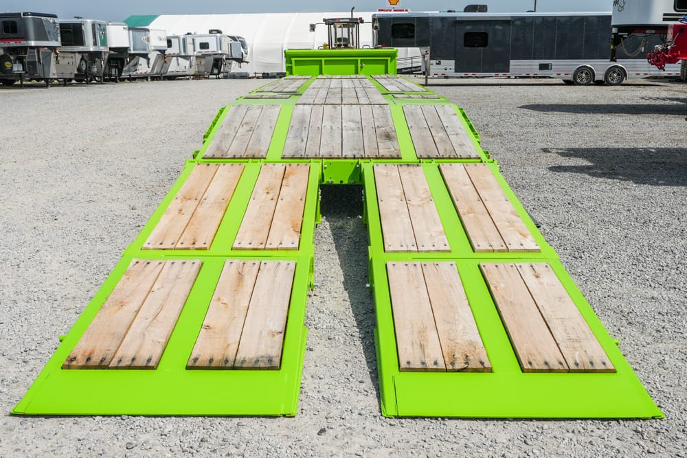 Bright lime-green flatbed trailer ramp with wooden planks, viewed from above in a gravel trailer lot.