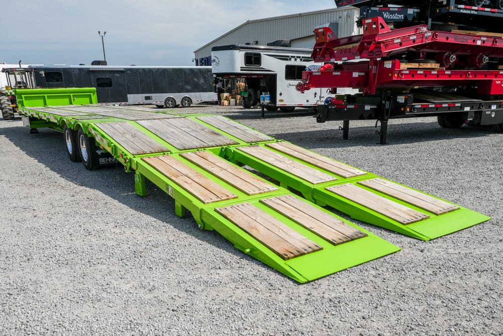 Bright lime-green flatbed trailer with wooden deck planks and dual loading ramps extending outward in a truck yard.